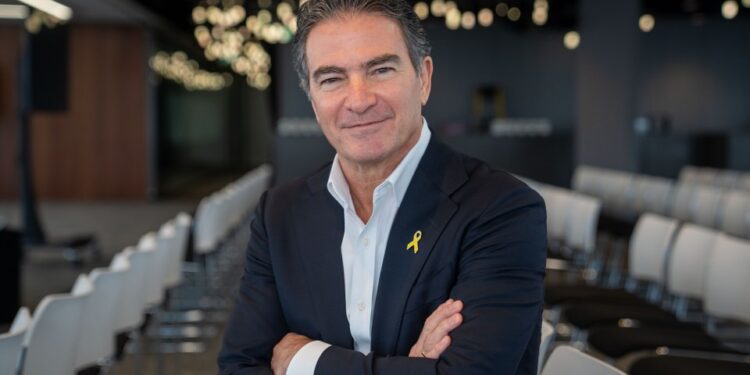 Yossi Cohen, ex jefe de Mossad, sonriendo con los brazos cruzados, con un traje con un alfiler amarillo.