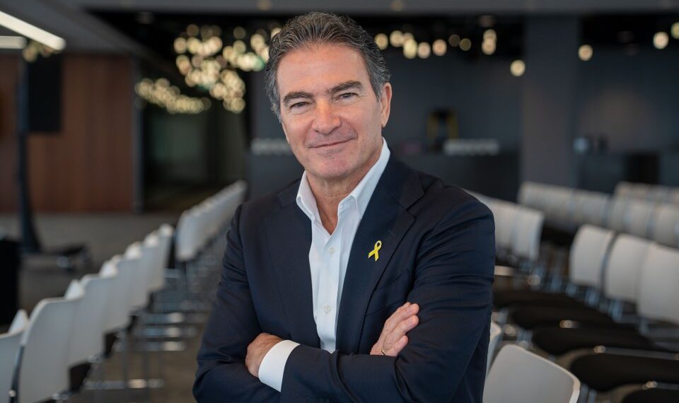 Yossi Cohen, ex jefe de Mossad, sonriendo con los brazos cruzados, con un traje con un alfiler amarillo.