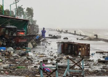 Un hombre en un impermeable que se encuentra en una carretera frente al mar de los escombros con grandes olas que se estrellan en el fondo debido al súper tifón Ragasa.