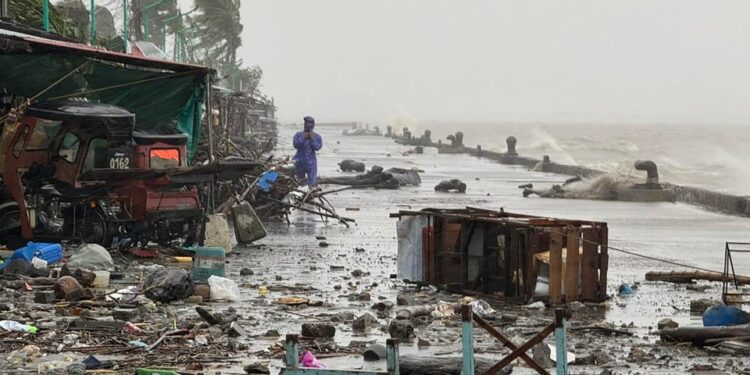Un hombre en un impermeable que se encuentra en una carretera frente al mar de los escombros con grandes olas que se estrellan en el fondo debido al súper tifón Ragasa.