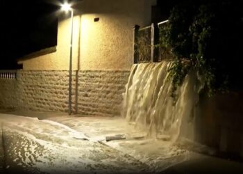Las aguas nocturnas en cascada sobre una pared en una calle, iluminadas por una luz de la calle.