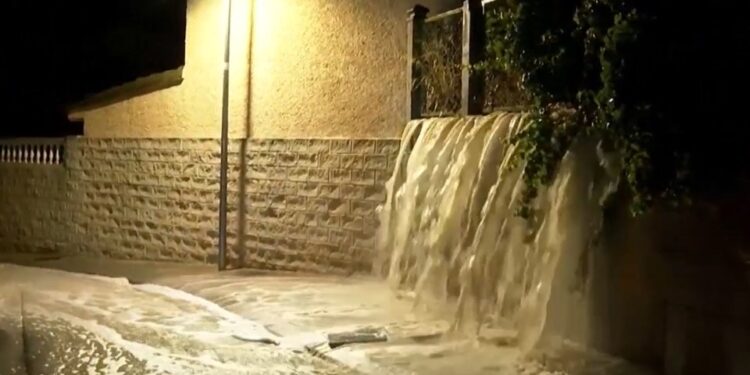 Las aguas nocturnas en cascada sobre una pared en una calle, iluminadas por una luz de la calle.