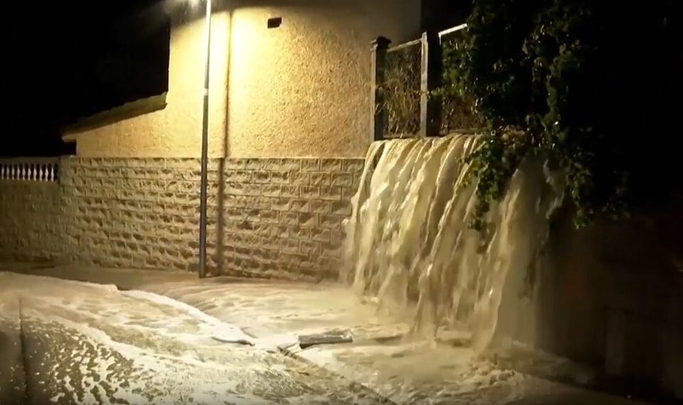 Las aguas nocturnas en cascada sobre una pared en una calle, iluminadas por una luz de la calle.