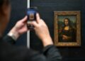 Persona fotografiando la Mona Lisa en el Museo del Louvre.