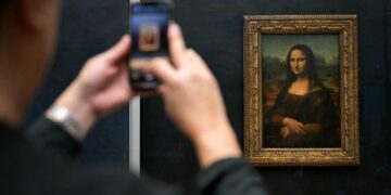 Persona fotografiando la Mona Lisa en el Museo del Louvre.