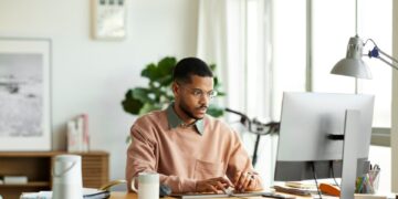 Un hombre que trabaja en una PC de escritorio en un escritorio de oficina en casa.