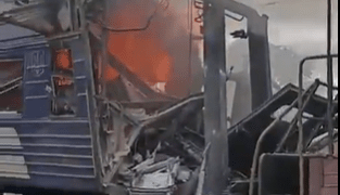 El vagón de tren dañado envuelto en llamas y humo.