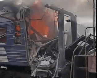 El vagón de tren dañado envuelto en llamas y humo.