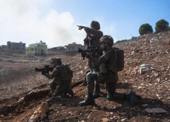 Tres soldados de la Brigada Golani realizan redadas en el sur del Líbano, con casas visibles al fondo.