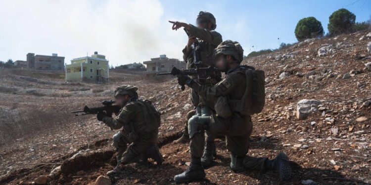 Tres soldados de la Brigada Golani realizan redadas en el sur del Líbano, con casas visibles al fondo.