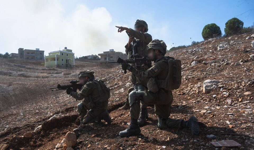 Tres soldados de la Brigada Golani realizan redadas en el sur del Líbano, con casas visibles al fondo.