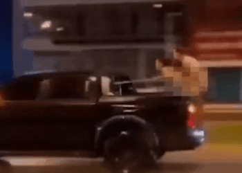 Una persona en la parte trasera de una camioneta en movimiento apunta a una pistola.