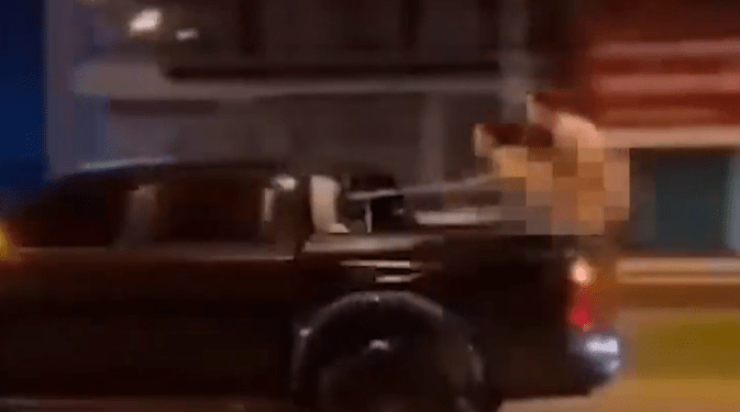 Una persona en la parte trasera de una camioneta en movimiento apunta a una pistola.