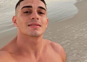 Flavio Augusto Schuller Azambuja sonriendo a la cámara con el océano y la playa detrás de él.