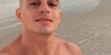 Flavio Augusto Schuller Azambuja sonriendo a la cámara con el océano y la playa detrás de él.