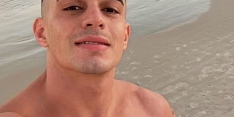 Flavio Augusto Schuller Azambuja sonriendo a la cámara con el océano y la playa detrás de él.