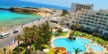 Una vista aérea de un complejo con dos piscinas, palmeras y un camino que conduce a una playa y al océano.
