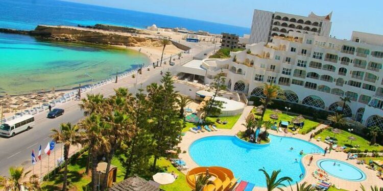 Una vista aérea de un complejo con dos piscinas, palmeras y un camino que conduce a una playa y al océano.