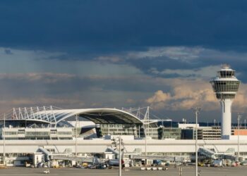 La torre de control de tráfico aéreo y el exterior del aeropuerto de Munich bajo un cielo oscuro y nublado.