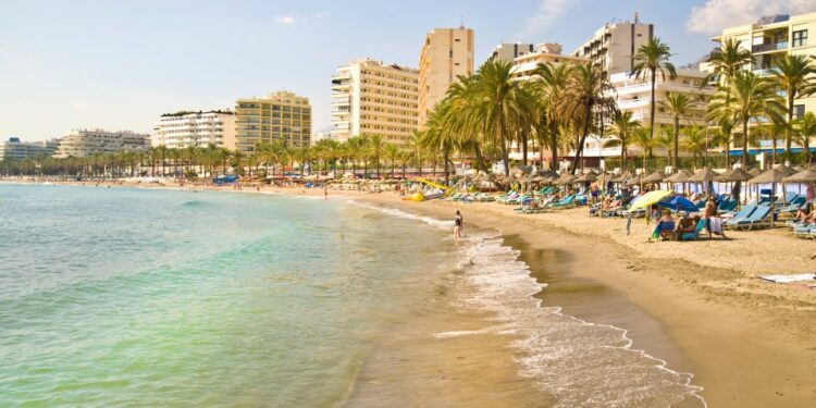 Playa turística en Marbella y Puerto Banús con palmeras, edificios y gente relajándose.