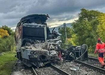 Una persona con un traje de seguridad rojo caminando cerca de los restos de un tren sobre las vías del tren.