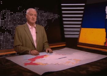 Un hombre presentando en un set de noticias con un mapa de Ucrania que muestra áreas de conflicto y una bandera rasgada de Ucrania y Rusia a la derecha.