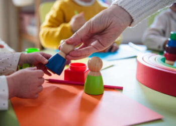 En un entorno de cuidado infantil, los niños juegan con juguetes y un adulto les entrega uno, concéntrese en las manos.