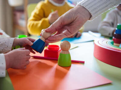 En un entorno de cuidado infantil, los niños juegan con juguetes y un adulto les entrega uno, concéntrese en las manos.