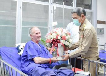 Vernon Unsworth, el salvador británico, recibe un ramo de flores en el hospital de manos de un funcionario tailandés.