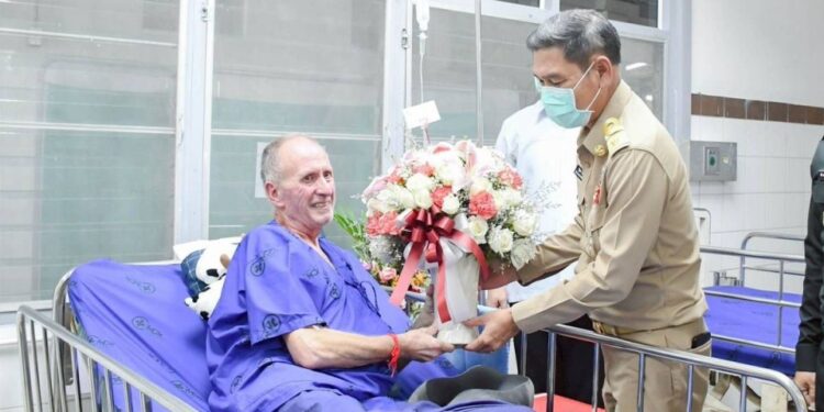 Vernon Unsworth, el salvador británico, recibe un ramo de flores en el hospital de manos de un funcionario tailandés.