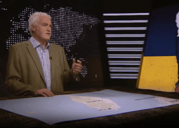 Un hombre que habla frente a un mapa mundial, con un mapa de banderas de Taiwán y Ucrania y Rusia.
