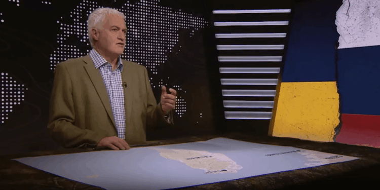 Un hombre que habla frente a un mapa mundial, con un mapa de banderas de Taiwán y Ucrania y Rusia.