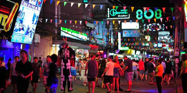 Gente caminando por Walking Street en Pattaya, Tailandia, por la noche, con luces de neón y coloridos banderines colgados encima.
