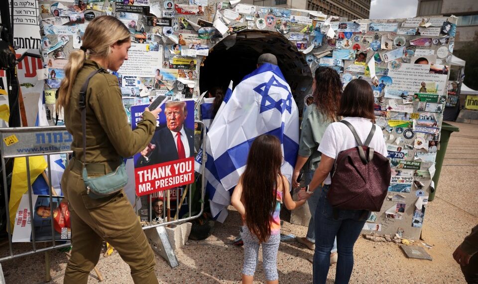 La gente visita la instalación de un túnel junto a un cartel de Donald Trump en "Plaza de los Rehenes" en Tel Aviv, Israel.
