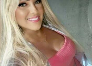 Una mujer sonriente con cabello largo y rubio y un top rosa.