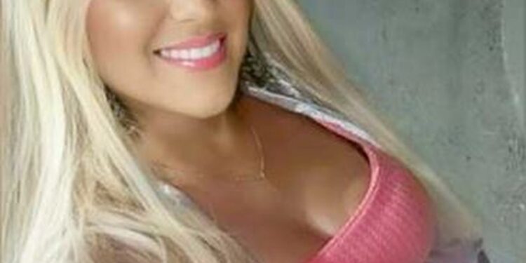 Una mujer sonriente con cabello largo y rubio y un top rosa.