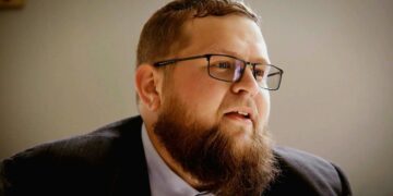 Un hombre con barba y gafas mirando hacia la derecha.