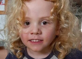 Primer plano de un niño pequeño con cabello rubio rizado y ojos marrones.