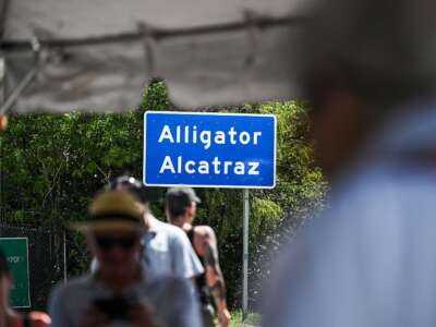 Las personas alrededor de un letrero de Alligator Alcatraz aparecen borrosas mientras el letrero permanece enfocado.