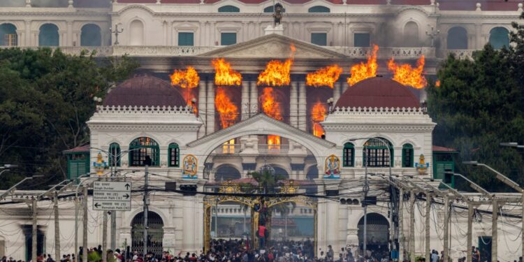 El fuego y el humo se elevan del Palacio Singha Durbar, que alberga edificios del gobierno y del Parlamento, a medida que los manifestantes se reúnen debajo durante las violentas manifestaciones en Katmandú.