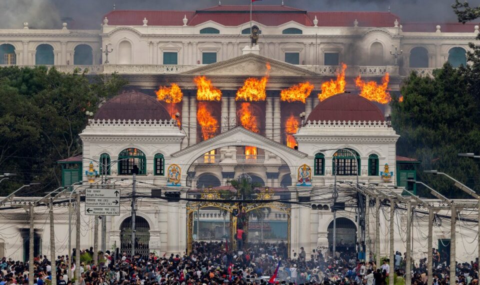 El fuego y el humo se elevan del Palacio Singha Durbar, que alberga edificios del gobierno y del Parlamento, a medida que los manifestantes se reúnen debajo durante las violentas manifestaciones en Katmandú.