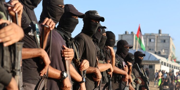 Militantes palestinos con pasamontañas y gorras negras hacen guardia con rifles automáticos.
