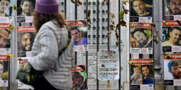 Una mujer pasa junto a una valla cubierta de carteles de rehenes israelíes, en su mayoría hombres, con las palabras "Tráelos a casa ahora" y "entführt" (secuestrado).