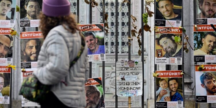 Una mujer pasa junto a una valla cubierta de carteles de rehenes israelíes, en su mayoría hombres, con las palabras "Tráelos a casa ahora" y "entführt" (secuestrado).