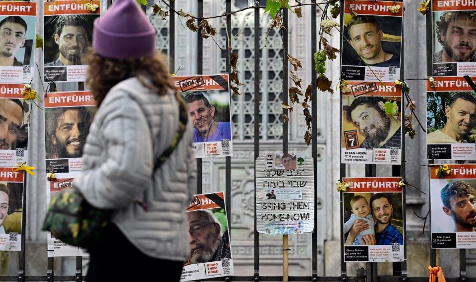 Una mujer pasa junto a una valla cubierta de carteles de rehenes israelíes, en su mayoría hombres, con las palabras "Tráelos a casa ahora" y "entführt" (secuestrado).