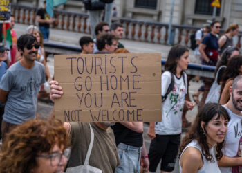 Manifestante sosteniendo un cartel que dice "Los turistas regresan a casa, no son bienvenidos."
