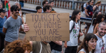 Manifestante sosteniendo un cartel que dice "Los turistas regresan a casa, no son bienvenidos."