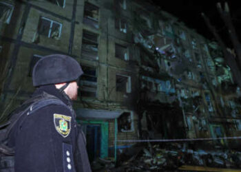 Un policía mira un edificio con una pared parcialmente destruida