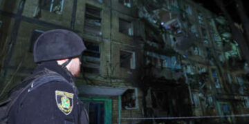 Un policía mira un edificio con una pared parcialmente destruida