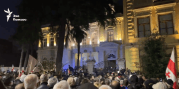 Los manifestantes se reunieron frente a un gran edificio iluminado por la noche, algunos sosteniendo banderas georgianas.